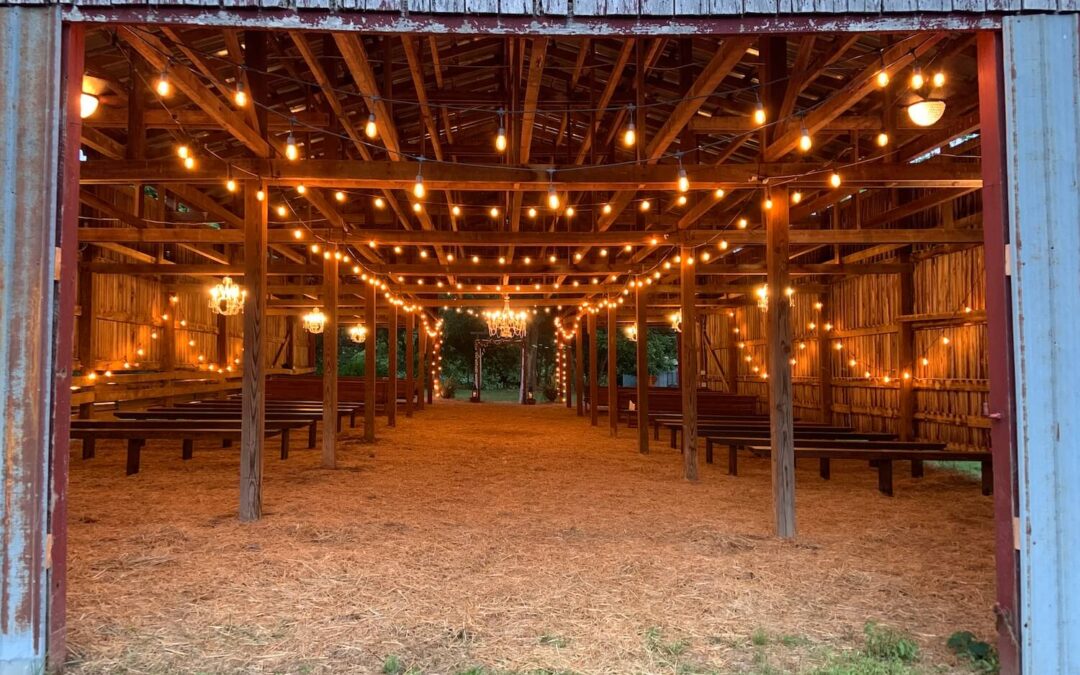 Long view of brides' approach from the front of the barn to the alter. All of the twinkle lights and chandeliers are lit.