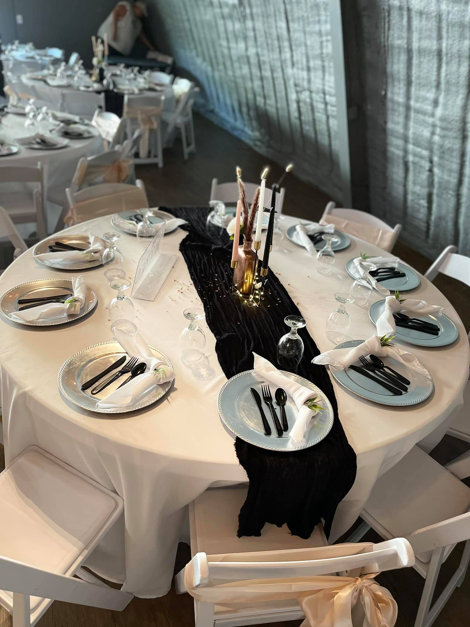 Photo of close up of round table set up with setting for 10 table runner over white tablecloths, wrapped chairs and candle centerpieces