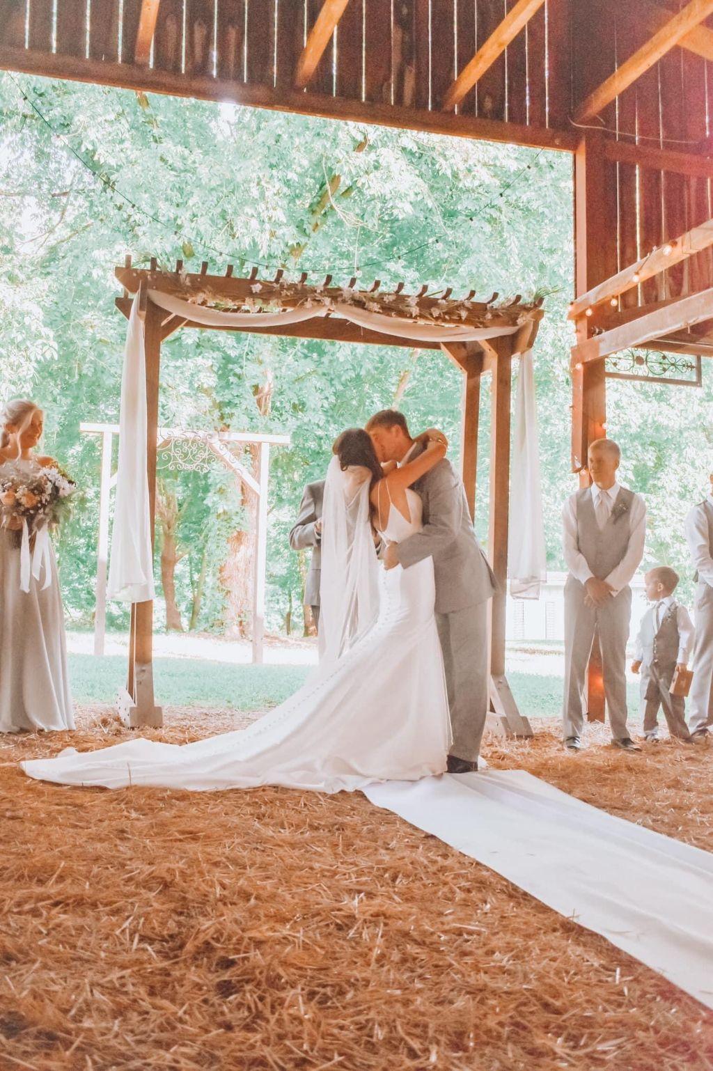 Burks wedding - photo of the kiss under the alter canopy of the barn with barn doors open to the woods