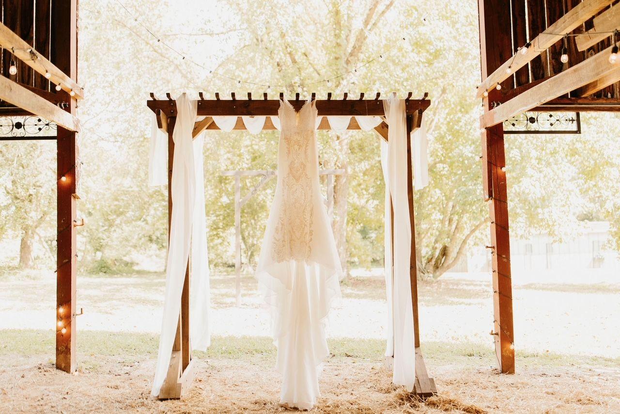 Photo fo the wedding alter with the wedding dress hanging in the front center of the alter with the sun shining through the open barn doors