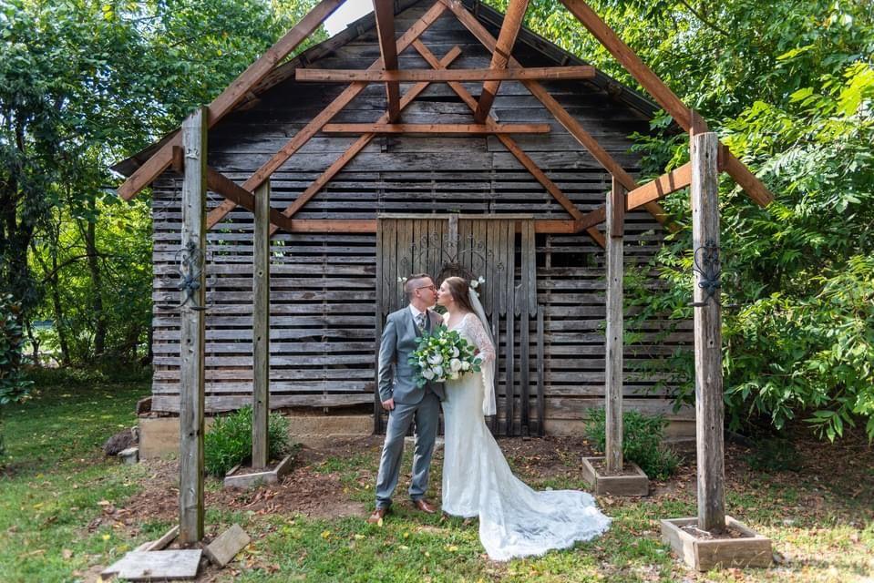 The couple share a kiss under the frame of the historic outbuilding on the grounds of Hayes House