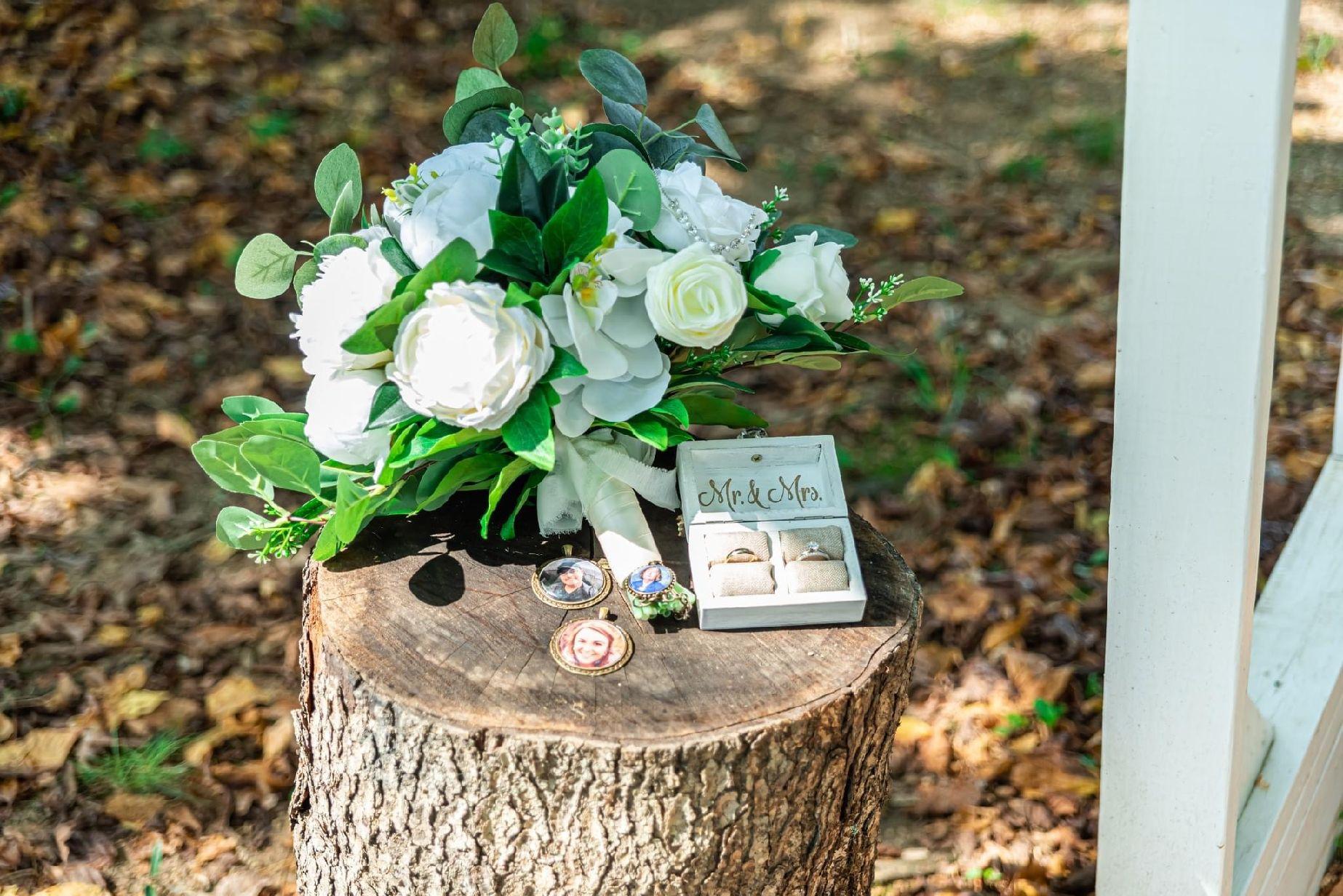 The bouquet of white roses and bright greenery are perched on a log with the couple's wedding bands and photo ornaments