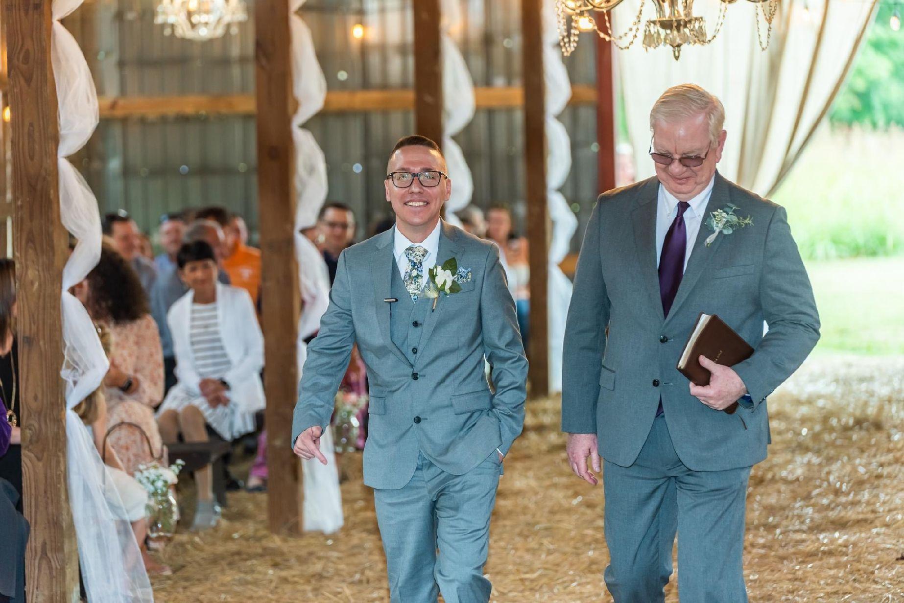 Dustin heads to the alter in a gray waisted tux with waist and tie with floral blue accents. The Boutonniere is a white lily.